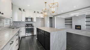 Kitchen featuring white cabinetry, sink, hanging light fixtures, stainless steel appliances, and a fireplace