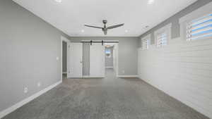 Unfurnished bedroom featuring carpet, ceiling fan, and a barn door