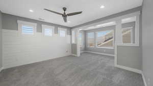 Empty room with wood walls, ceiling fan, a healthy amount of sunlight, and light carpet