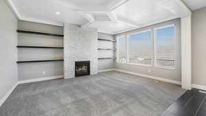 Unfurnished living room with carpet flooring, built in shelves, and a stone fireplace