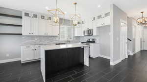 Kitchen with white cabinets, a notable chandelier, a kitchen island, and stainless steel appliances