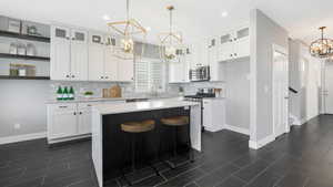 Kitchen with white cabinetry, sink, stainless steel appliances, a notable chandelier, and a kitchen island