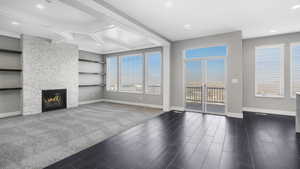 Unfurnished living room featuring a fireplace, beamed ceiling, built in features, and dark wood-type flooring