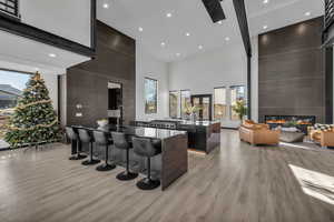 Kitchen featuring dark brown cabinetry, a towering ceiling, an island with sink, a breakfast bar area, and a fireplace