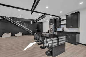 Kitchen with light hardwood / wood-style flooring, decorative backsplash, appliances with stainless steel finishes, a kitchen island, and a breakfast bar area