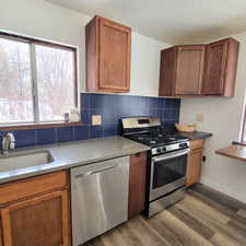 Kitchen with sink, appliances with stainless steel finishes, backsplash, and wood-type flooring