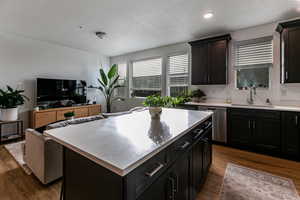 Kitchen featuring sink, stainless steel dishwasher, a textured ceiling, a kitchen island, and dark hardwood / wood-style flooring