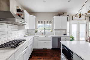 Kitchen featuring dark wood-type flooring, wall chimney range hood, sink, appliances with stainless steel finishes, and white cabinetry