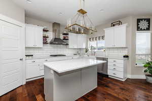 Kitchen featuring a center island, wall chimney exhaust hood, dark hardwood / wood-style floors, appliances with stainless steel finishes, and white cabinetry