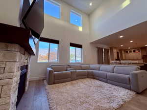 Living room featuring a stone fireplace, light wood-type flooring, and a towering ceiling