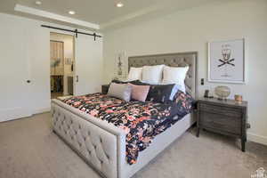 Carpeted bedroom with a barn door, a tray ceiling, and ensuite bath