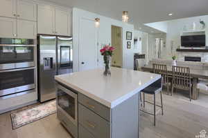 Kitchen featuring light hardwood / wood-style floors, pendant lighting, gray cabinets, a kitchen island, and appliances with stainless steel finishes