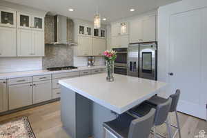 Kitchen featuring decorative light fixtures, stainless steel appliances, light hardwood / wood-style floors, and wall chimney range hood