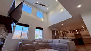 Living room featuring ceiling fan, a fireplace, a towering ceiling, and light hardwood / wood-style flooring