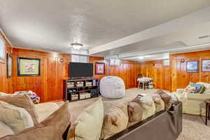 Carpeted living room featuring wood walls and a textured ceiling