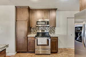 Kitchen featuring backsplash, light stone countertops, and stainless steel appliances