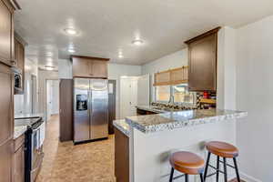 Kitchen with kitchen peninsula, appliances with stainless steel finishes, a kitchen breakfast bar, light stone counters, and sink