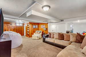 Living room featuring wood walls, a textured ceiling, and light carpet