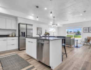 Kitchen featuring white cabinetry, stainless steel appliances, an island with sink, pendant lighting, and light wood-type flooring