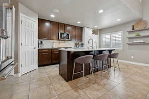 Kitchen featuring stainless steel appliances, tasteful backsplash, a breakfast bar area, a kitchen island with sink, and dark brown cabinets