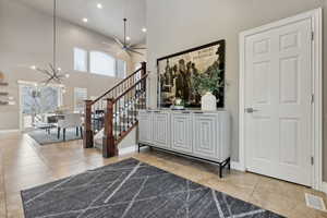 Entrance foyer featuring ceiling fan with notable chandelier, light tile patterned floors, a towering ceiling, and plenty of natural light