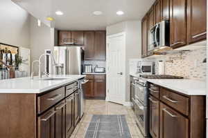 Kitchen with a center island with sink, sink, decorative backsplash, premium appliances, and light tile patterned flooring