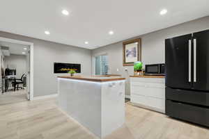 Kitchen with white cabinetry, black fridge, a center island, and light wood-type flooring