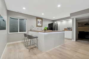 Kitchen featuring kitchen peninsula, light wood-type flooring, a breakfast bar, stainless steel appliances, and white cabinetry