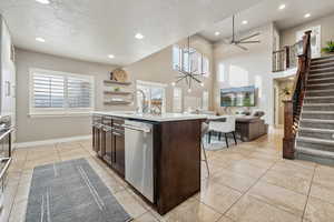 Kitchen featuring dark brown cabinetry, a wealth of natural light, a center island with sink, and stainless steel dishwasher