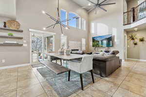 Dining space with a high ceiling, ceiling fan with notable chandelier, a stone fireplace, and plenty of natural light