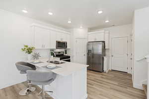 Kitchen featuring a breakfast bar, white cabinetry, stainless steel appliances, and light hardwood / wood-style flooring