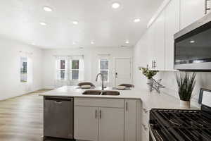 Kitchen with appliances with stainless steel finishes, light hardwood / wood-style floors, white cabinetry, and sink