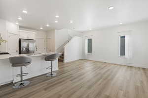 Kitchen featuring sink, stainless steel fridge with ice dispenser, light hardwood / wood-style floors, a breakfast bar area, and white cabinets