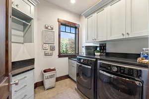 Clothes washing area with separate washer and dryer, light tile patterned floors, and cabinets