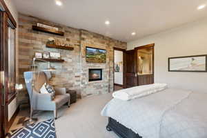 Bedroom featuring light carpet, ensuite bath, and a stone fireplace