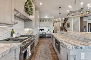 Kitchen featuring light stone countertops, decorative backsplash, dark wood-type flooring, and appliances with stainless steel finishes