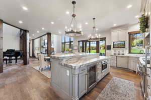 Kitchen with hardwood / wood-style floors, wine cooler, decorative light fixtures, a large island, and light stone counters