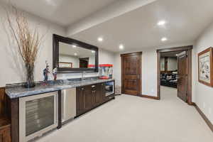 Bar with dark brown cabinetry, light colored carpet, stainless steel appliances, sink, and wine cooler