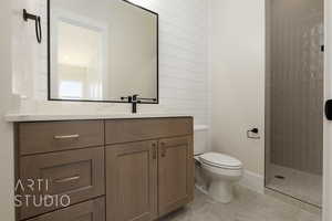 Bathroom featuring tile patterned floors, a tile shower, vanity, wooden walls, and toilet