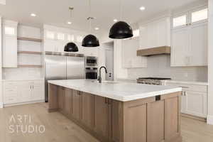 Kitchen featuring white cabinets, a spacious island, built in appliances, and light wood-type flooring