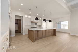 Kitchen with sink, a large island with sink, beam ceiling, light hardwood / wood-style floors, and white cabinetry