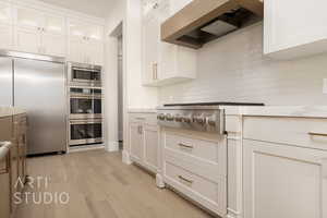 Kitchen featuring backsplash, light hardwood / wood-style flooring, built in appliances, custom range hood, and white cabinetry