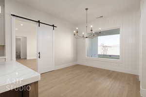 Unfurnished dining area with a barn door, light hardwood / wood-style floors, an inviting chandelier, and wood walls