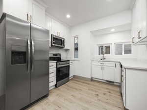 Kitchen with sink, white cabinets, stainless steel appliances, and light hardwood / wood-style flooring