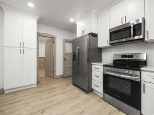 Kitchen with light hardwood / wood-style flooring, white cabinets, and stainless steel appliances