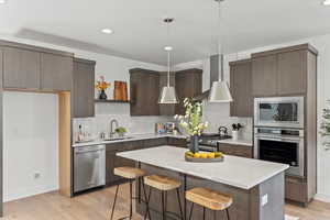 Kitchen featuring pendant lighting, wall chimney exhaust hood, stainless steel appliances, sink, and light hardwood / wood-style flooring