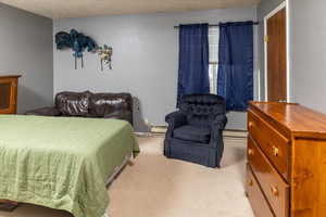 Carpeted bedroom with a textured ceiling and a baseboard radiator