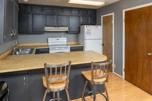 Kitchen with sink, kitchen peninsula, white appliances, a breakfast bar area, and light wood-type flooring