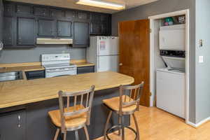 Kitchen featuring light hardwood / wood-style floors, a textured ceiling, white appliances, a kitchen bar, and stacked washer and clothes dryer