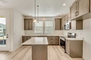 Kitchen featuring decorative light fixtures, a kitchen island, appliances with stainless steel finishes, and light hardwood / wood-style flooring